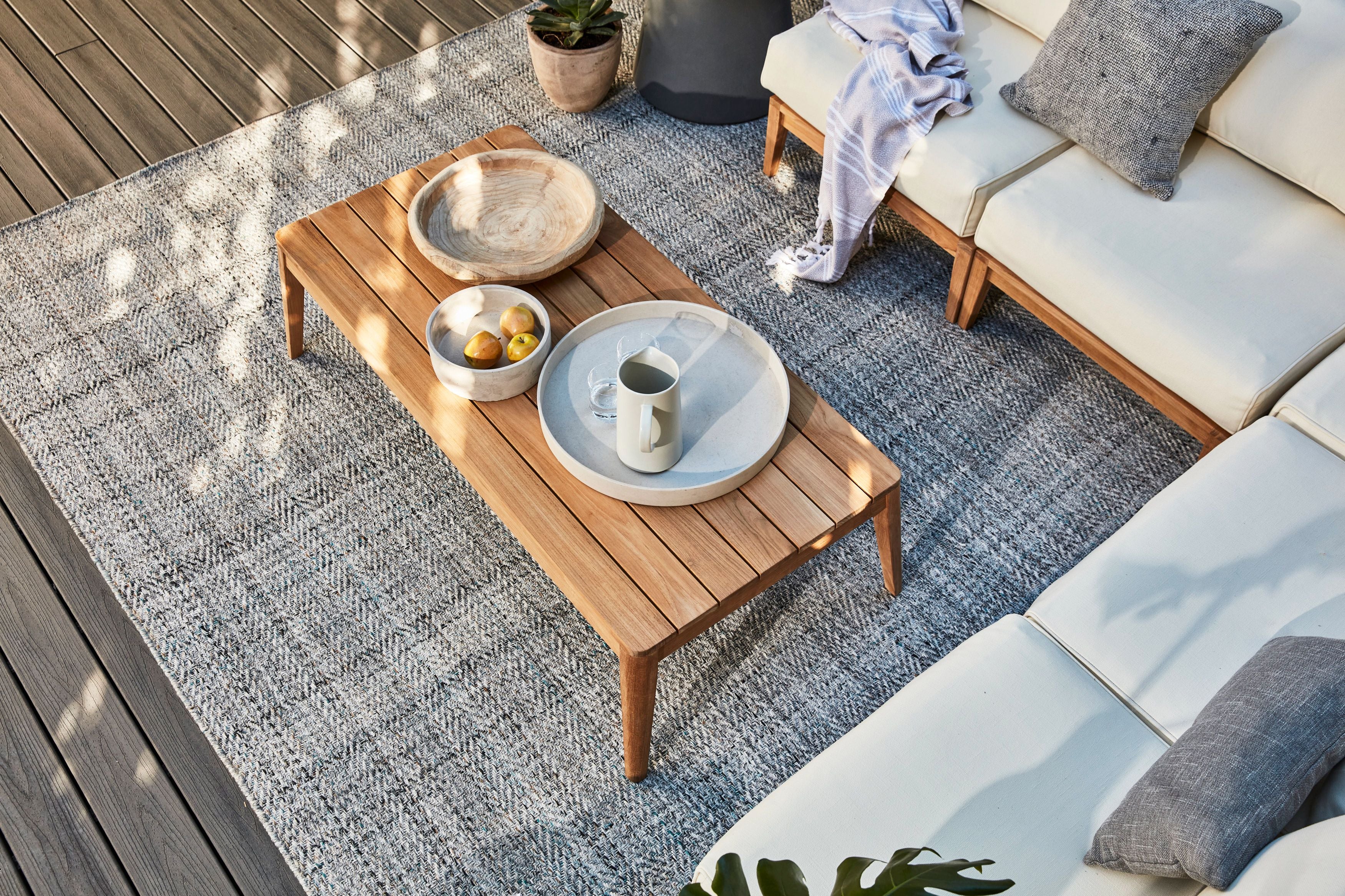 Outdoor rug beneath a wooden coffee table and cushioned seating on a patio deck