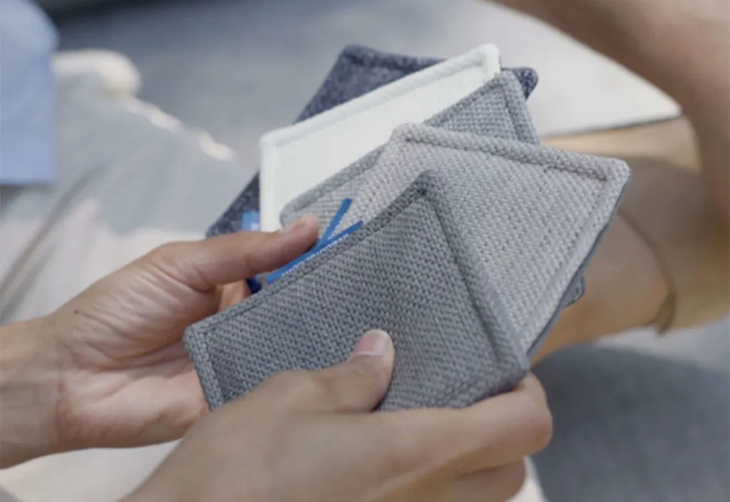 Hands holding a set of gray and neutral fabric swatches for outdoor furniture, showing different textures and shades
