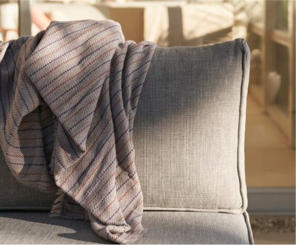 Gray fabric cushion with a folded throw draped over the backrest, showing everyday outdoor use
