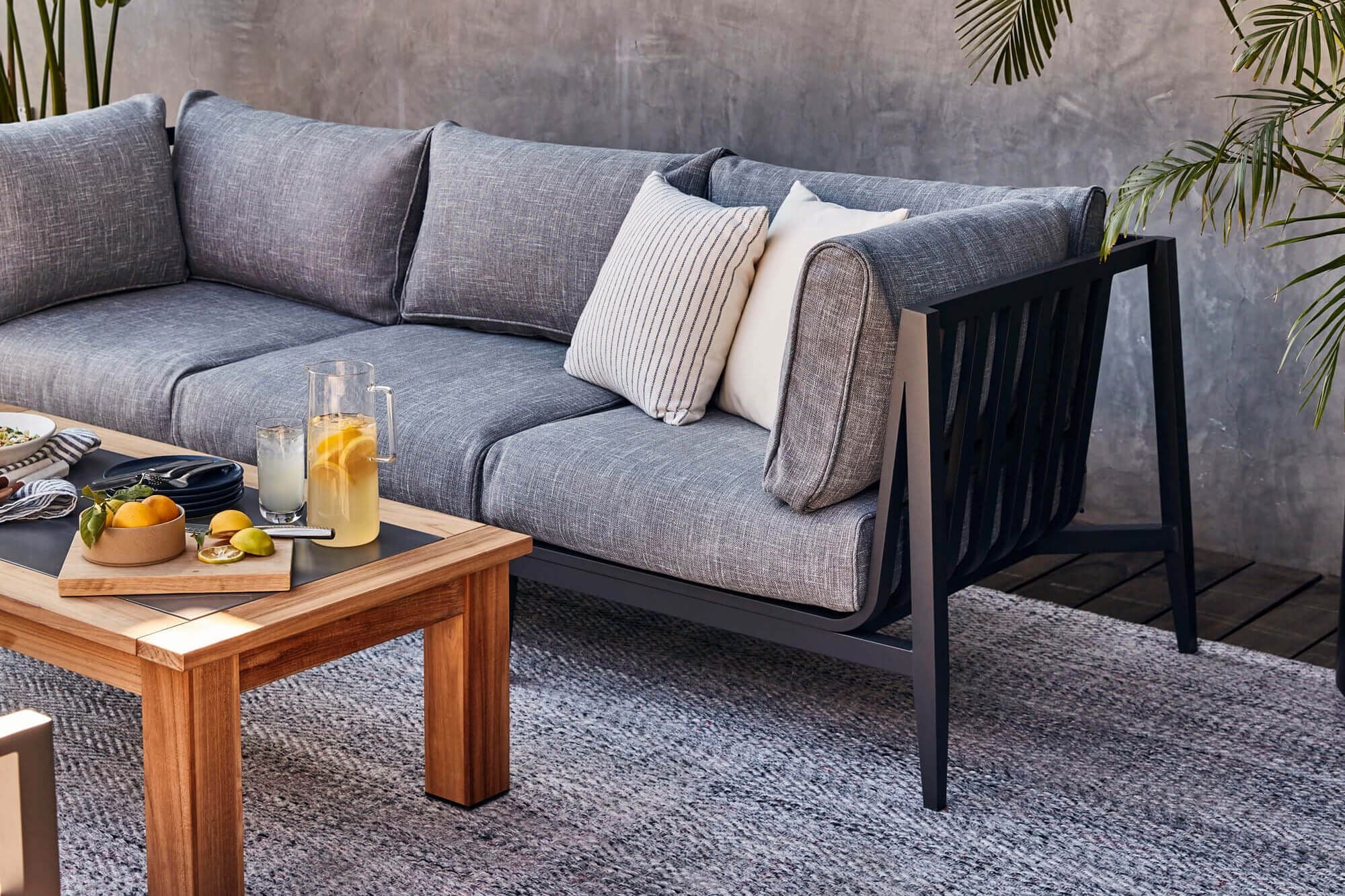 A closeup of the charcoal aluminum outdoor sofa showing the detail of the pacific fog gray fabric and the pebble gray outdoor rug it's sitting on.