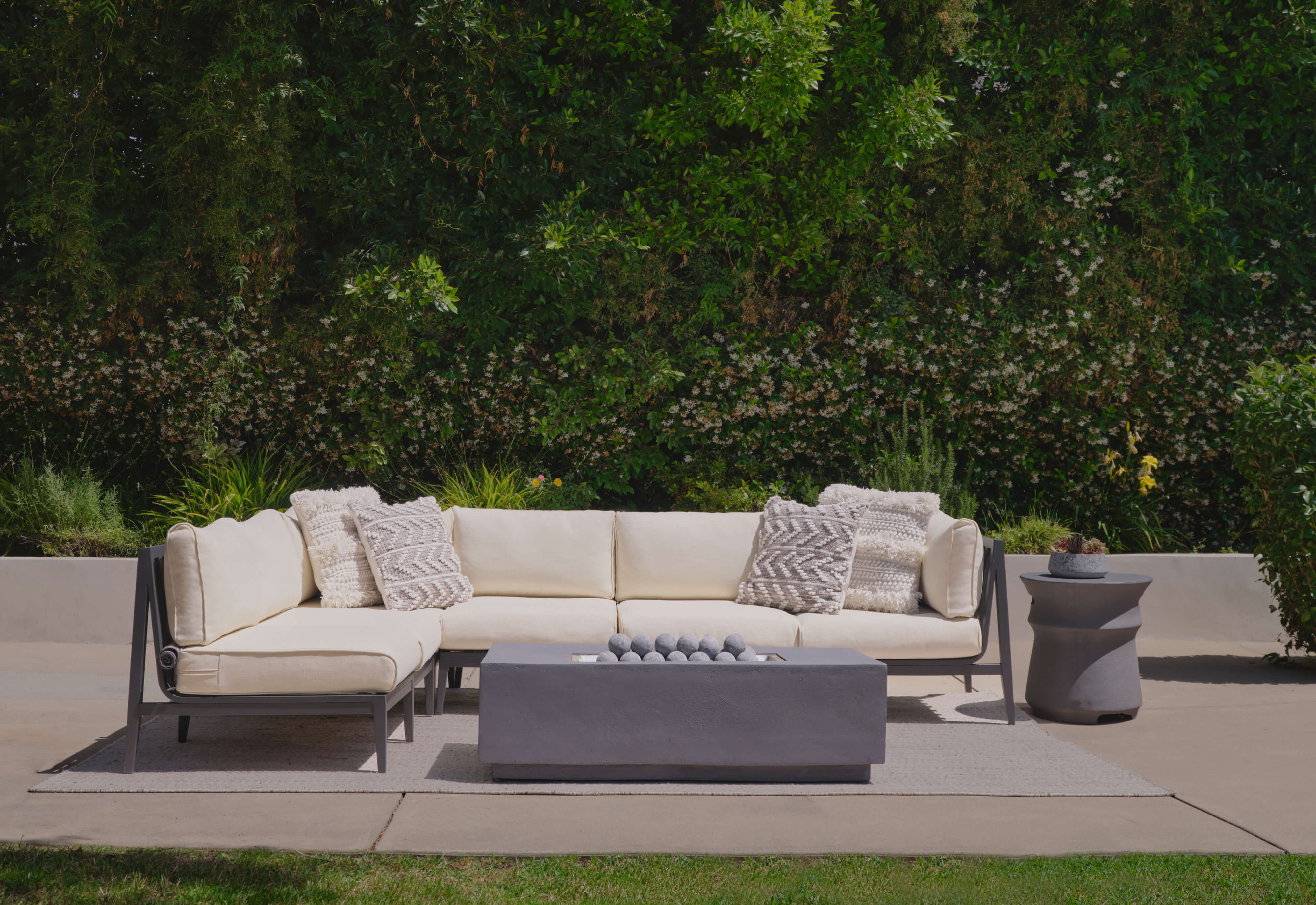 Charcoal aluminum L sectional with palisades cream cushions shown with the fire pit and classic concrete side table.