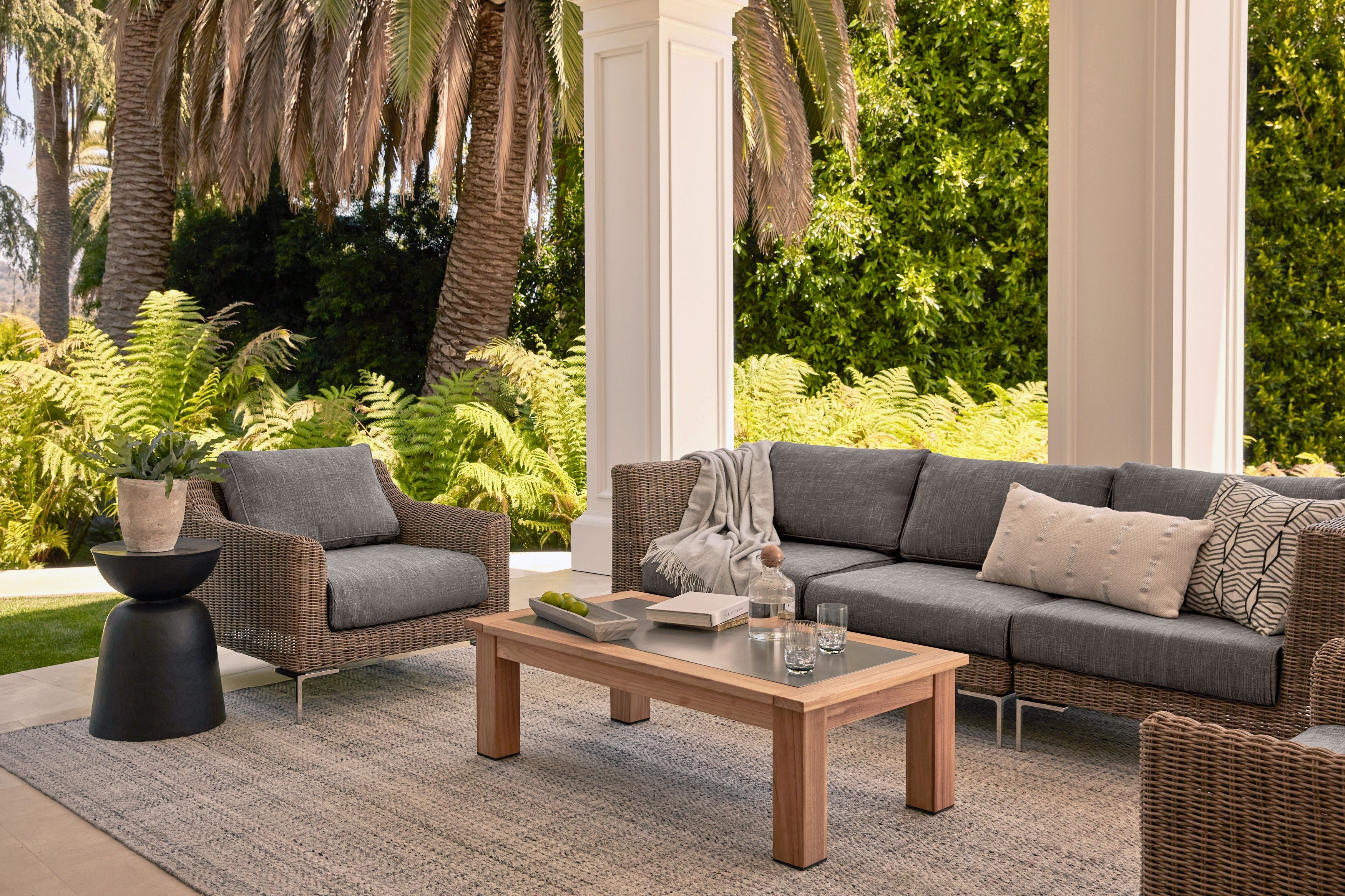 Three seat brown wicker outdoor sofa with armchair featured on a patio with dark pebble gray fabric. 