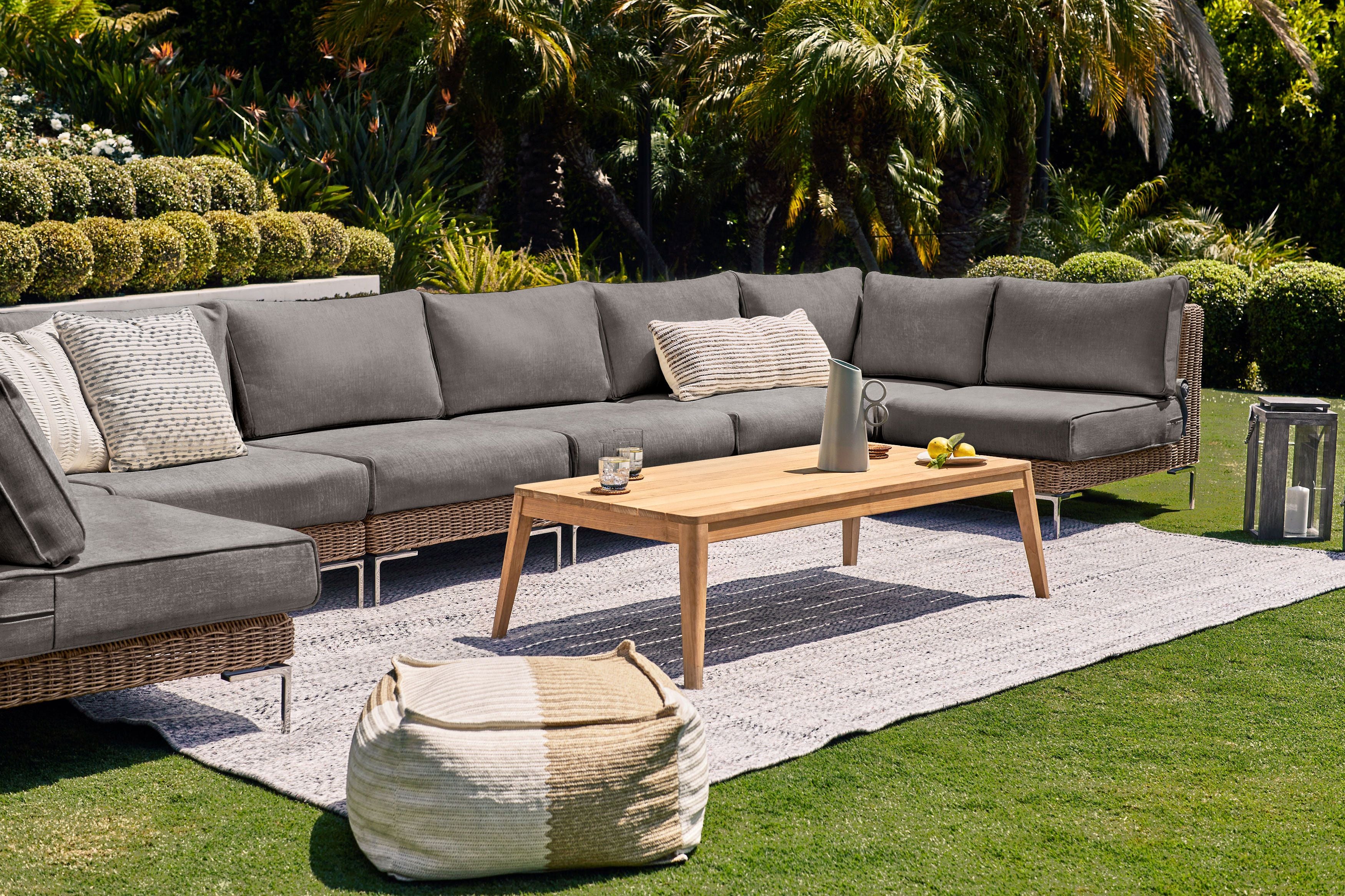 The 8 seat U sectional in brown wicker shown in a backyard with our tapered leg teak coffee table and seashell gray rug. 