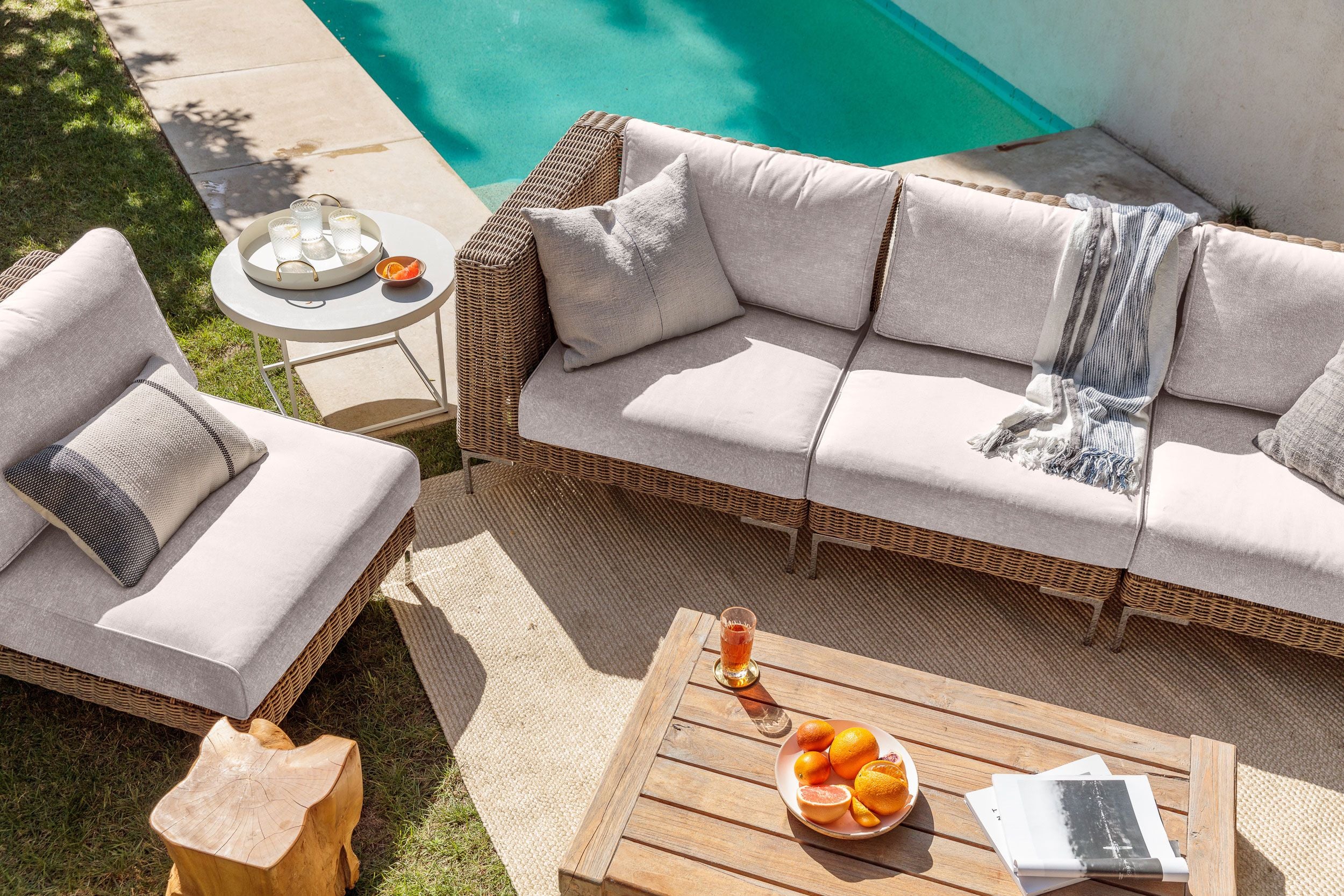 The 3 seat brown wicker sofa in sandstone gray with single armless chair shown poolside on a sunny day. 